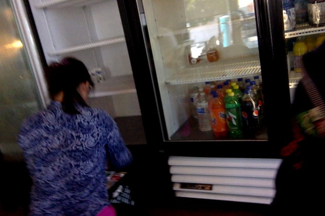 Happy Donut worker or co-owner restocking milk to cold case on her last day here in Palo Alto